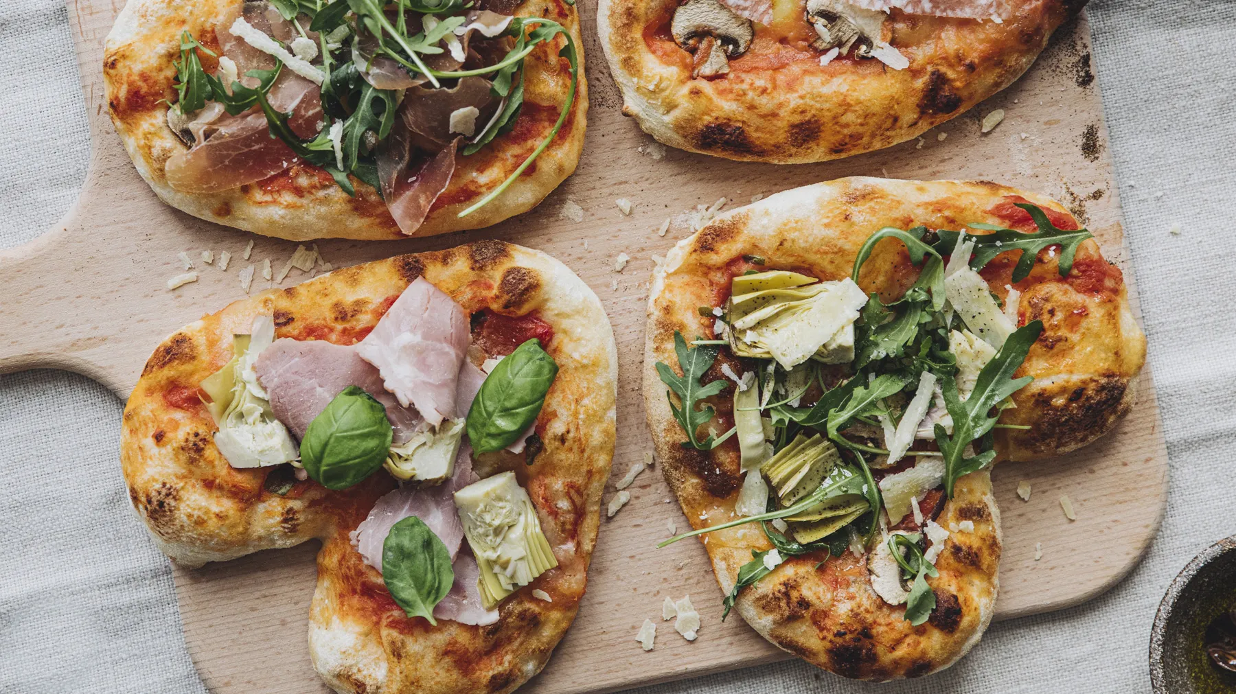 Vier herzförmige Pizzen mit verschiedenen Belägen auf einem Holzbrett