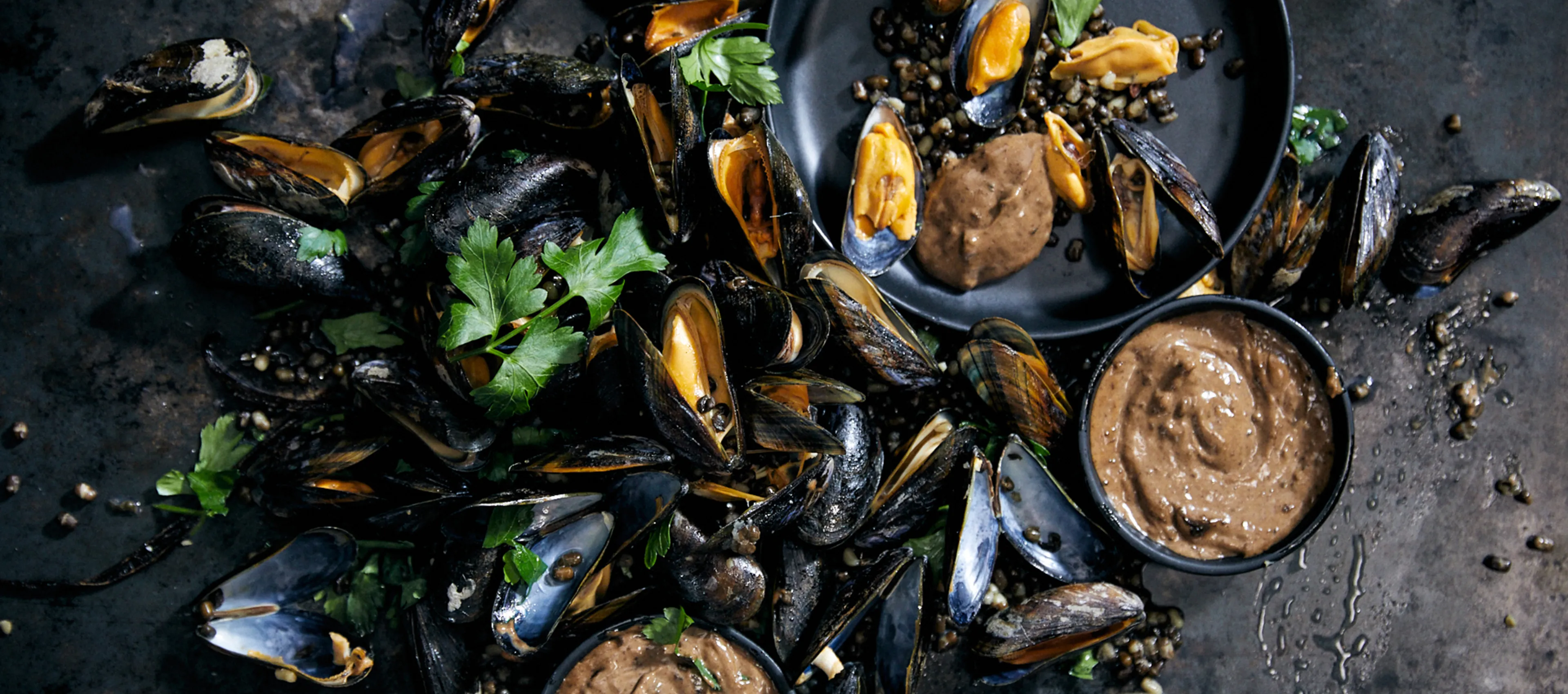 Mussels, sauces, and herbs on a dark background, creating a visually appealing seafood dish.