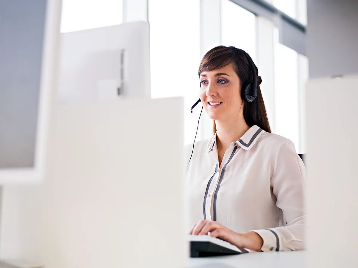 אישה עם אוזניות יושבת מול מחשבים במשרד, מתמקדת בעבודתה עם מסכים נוספים ברקע.