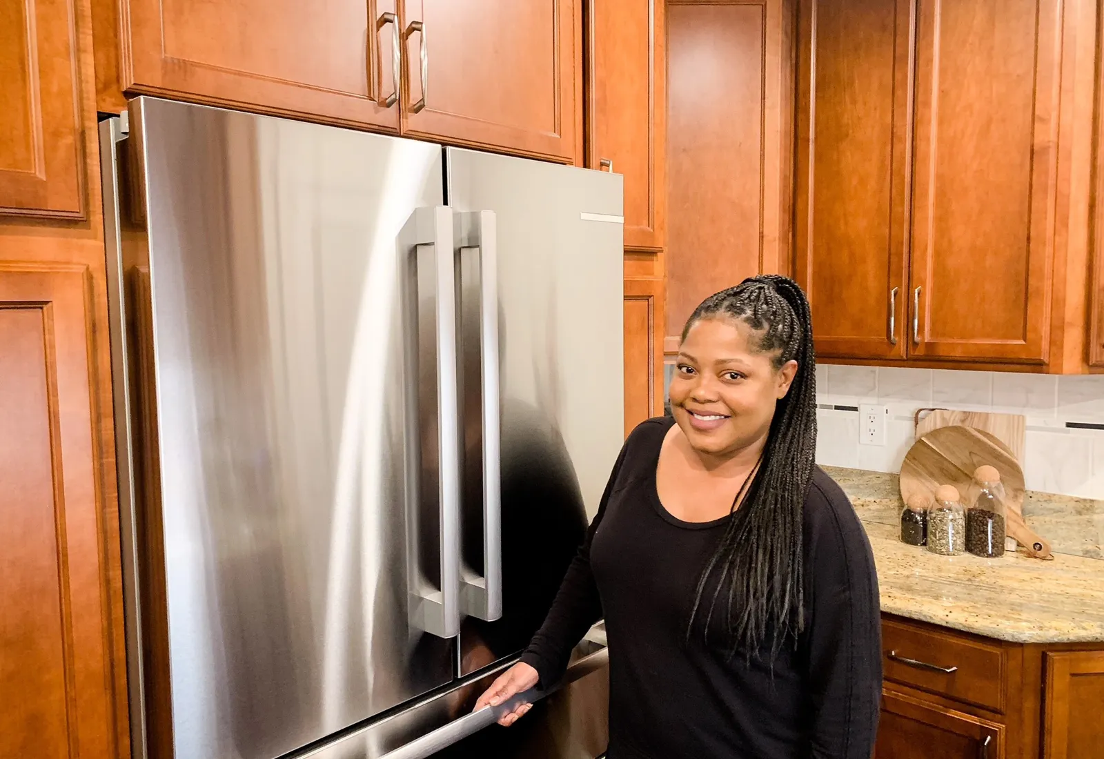 Woman smiling in kitchen with Bosch stainless steel fridge under wooden cabinets.