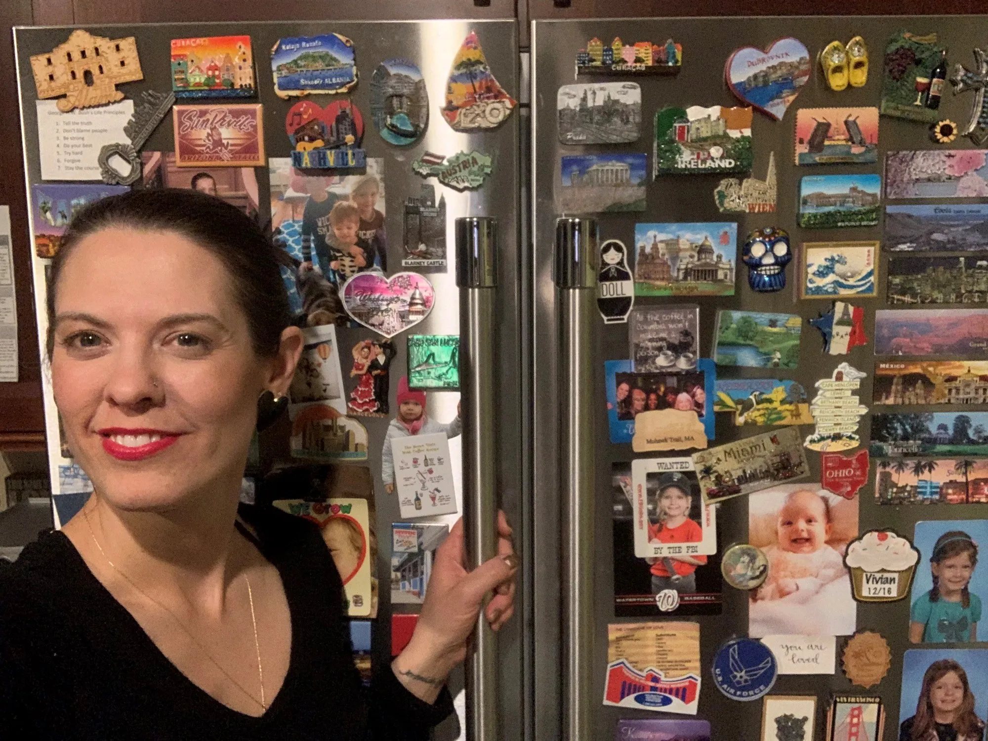 Woman smiling in front of a Bosch fridge covered with travel-themed magnets and photos.