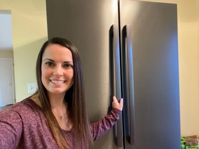 Woman smiling next to a large Bosch stainless steel refrigerator with double doors.