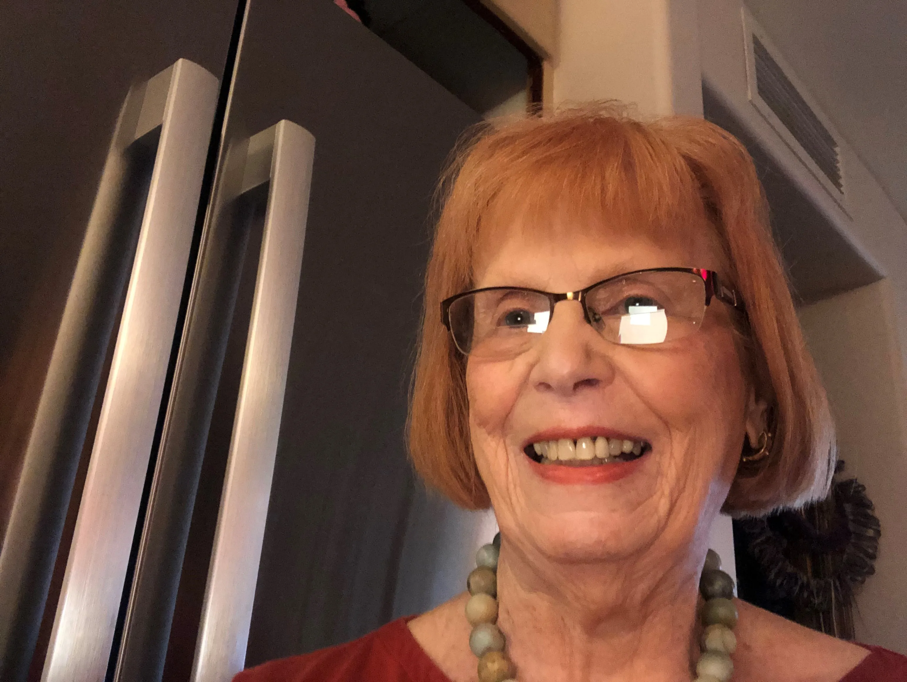 A smiling woman with glasses stands by a Bosch stainless steel refrigerator.