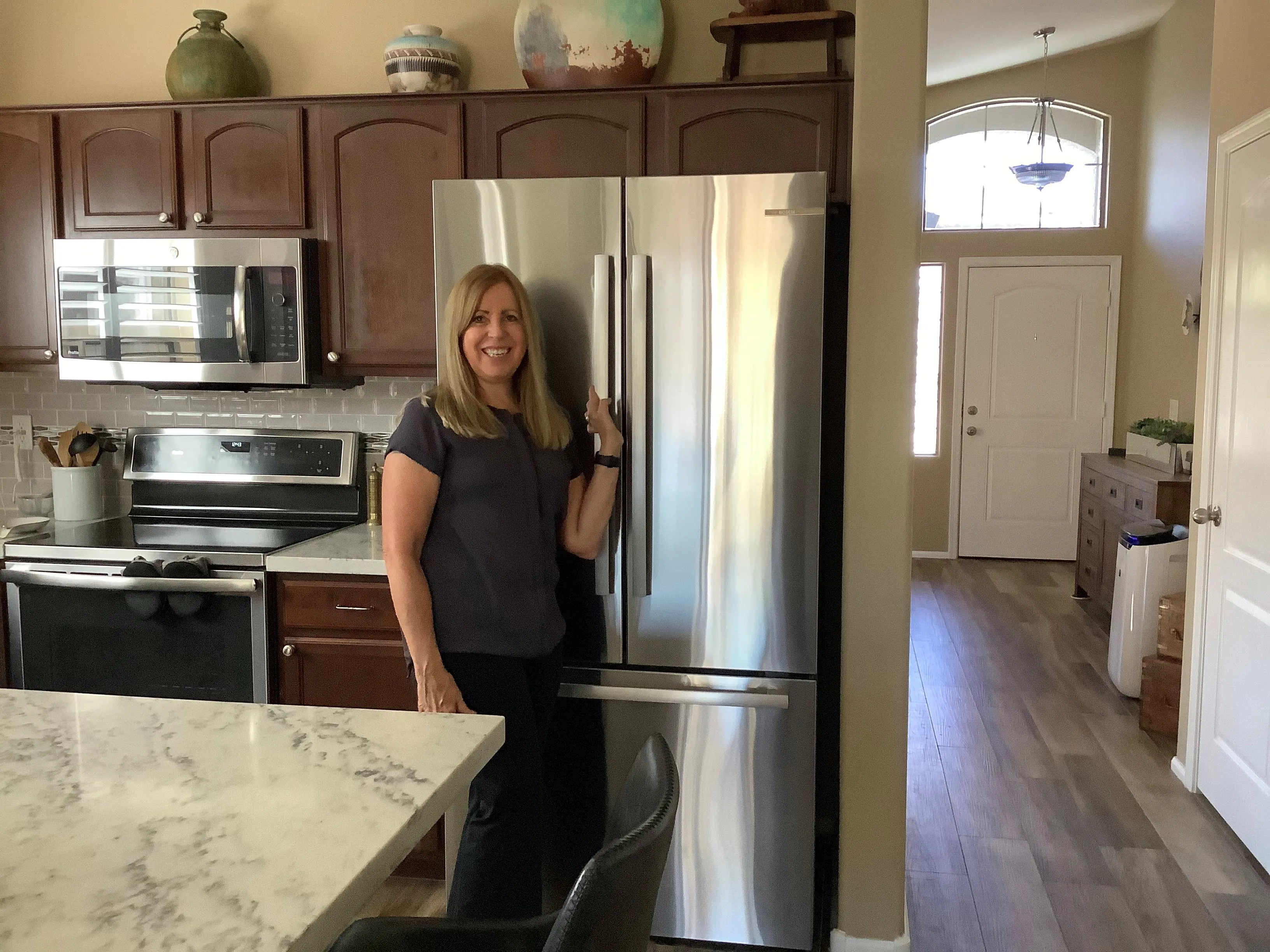 A woman standing beside a Bosch stainless steel refrigerator in a modern kitchen.
