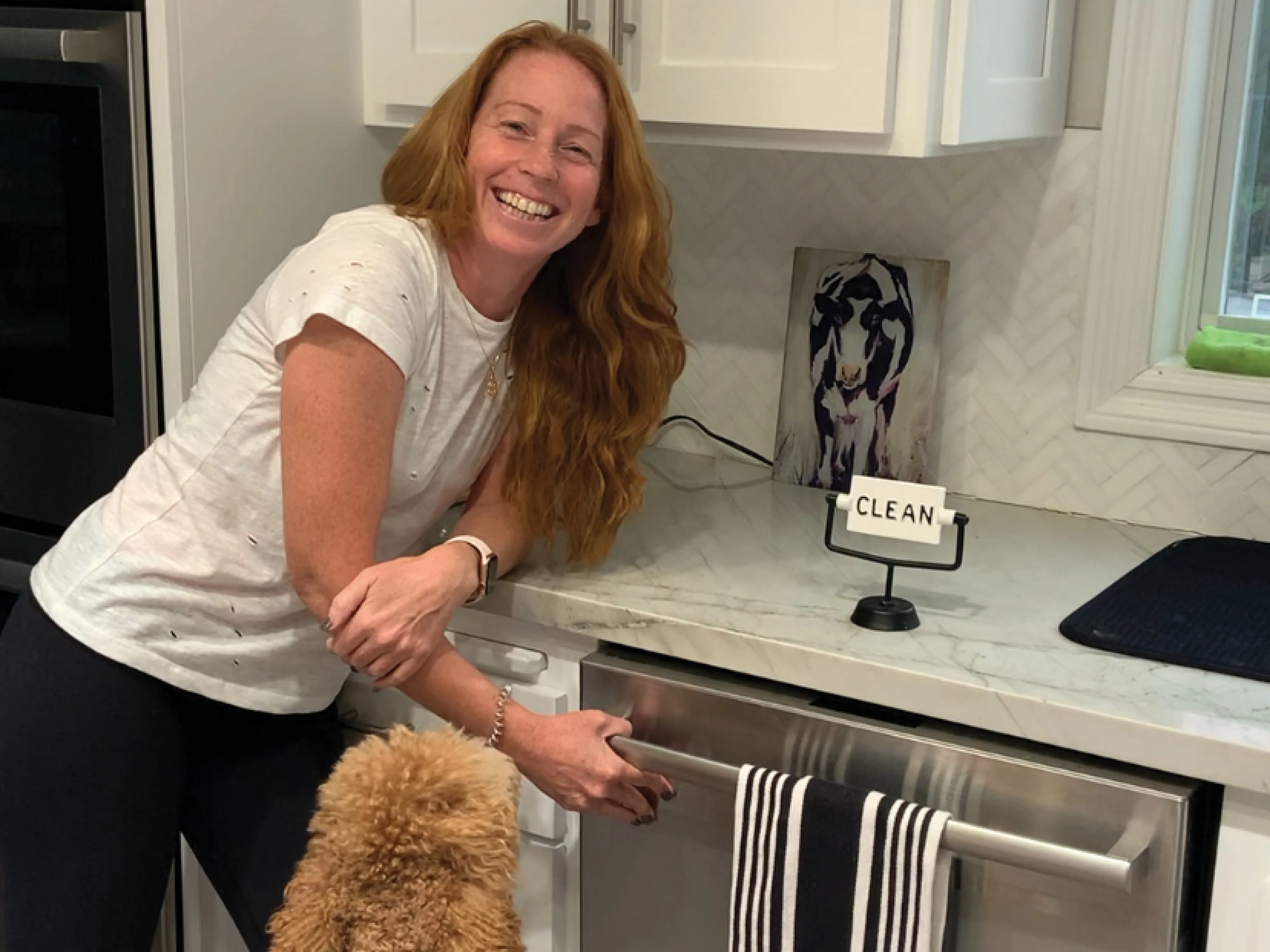 Woman smiling next to an open Bosch dishwasher with a 'clean' sign on the counter.