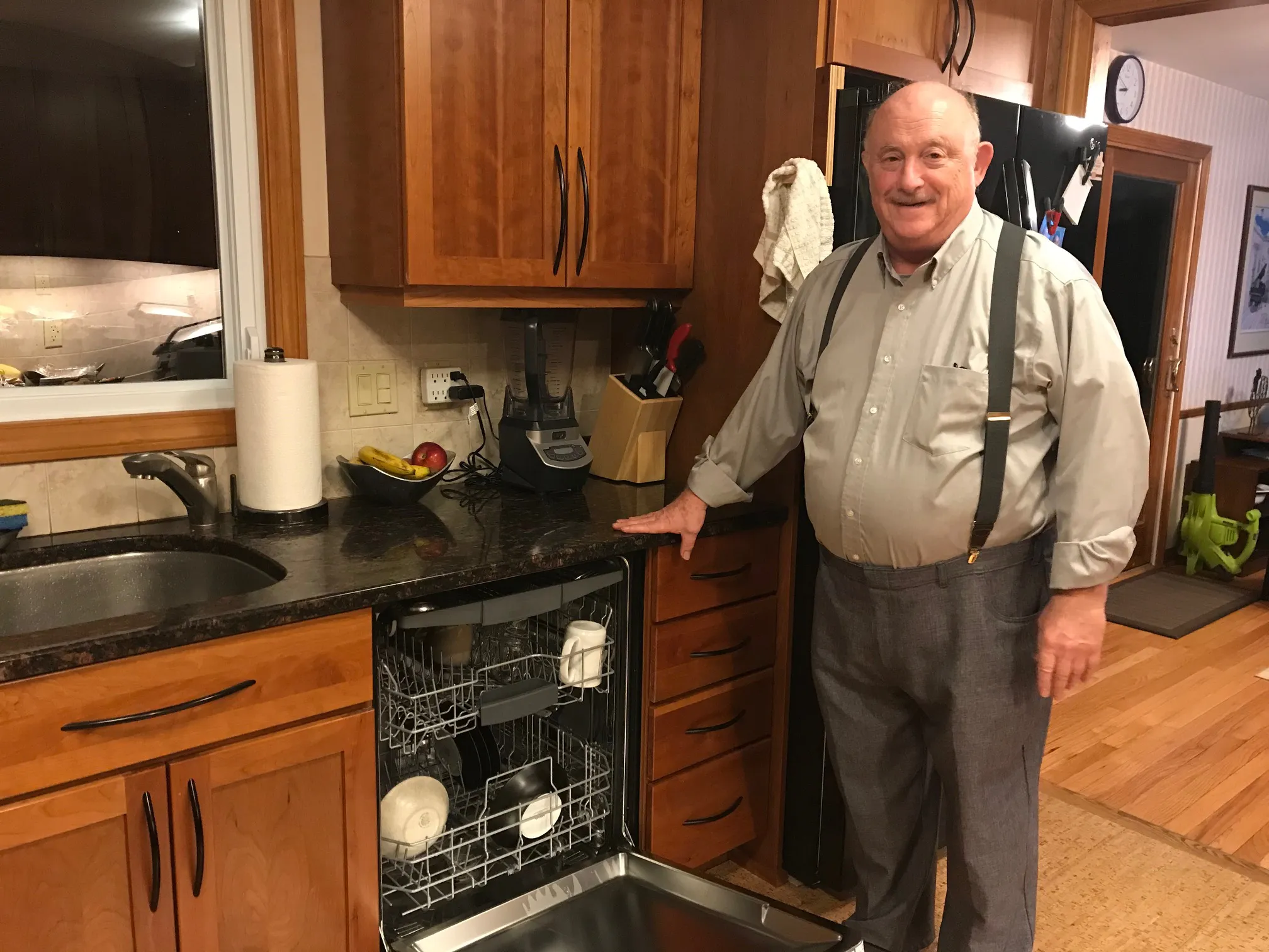 Man in kitchen standing beside an open Bosch dishwasher with wooden cabinetry and counter space.