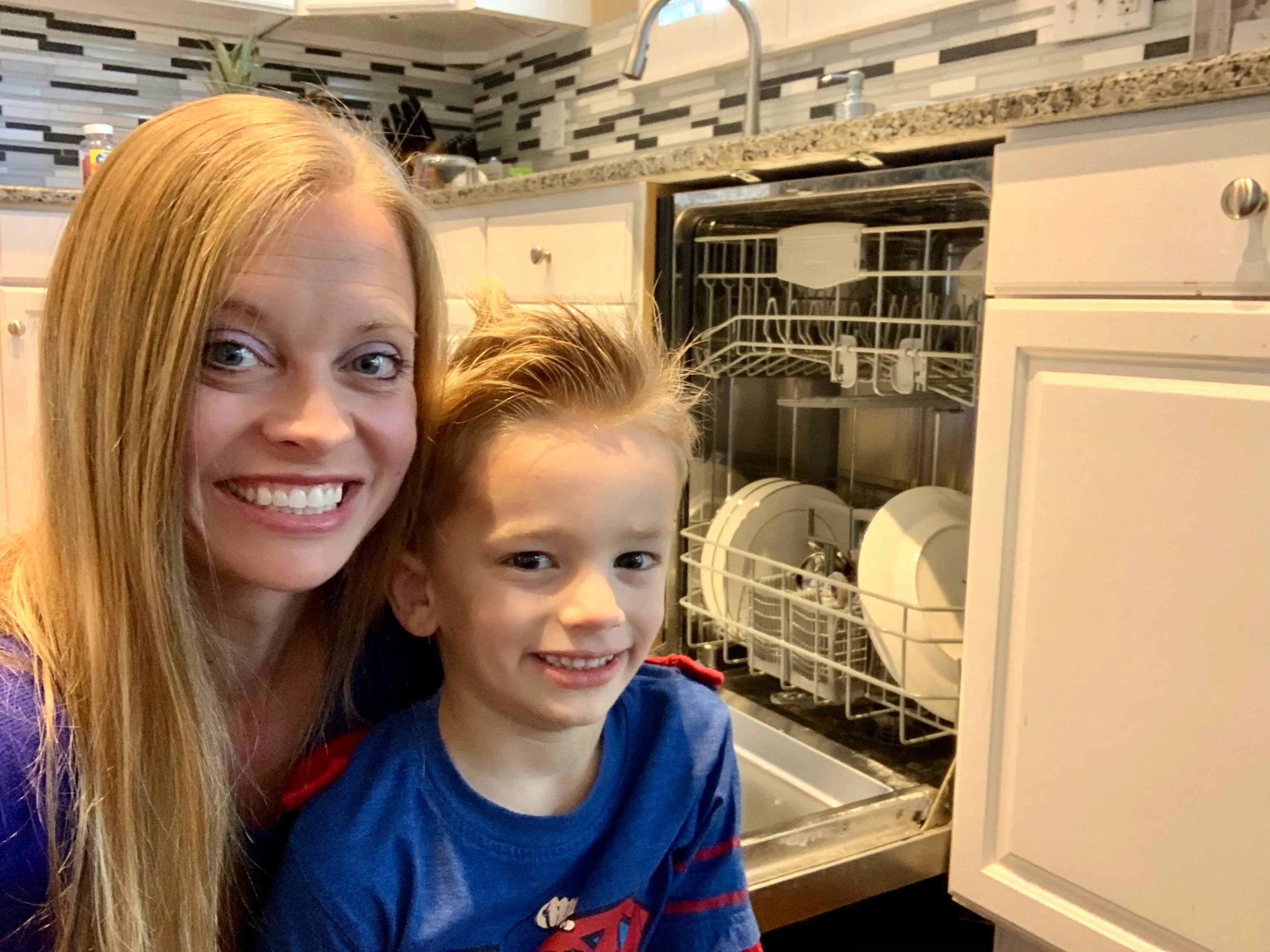Smiling woman and child near an open Bosch dishwasher in a modern kitchen setting.