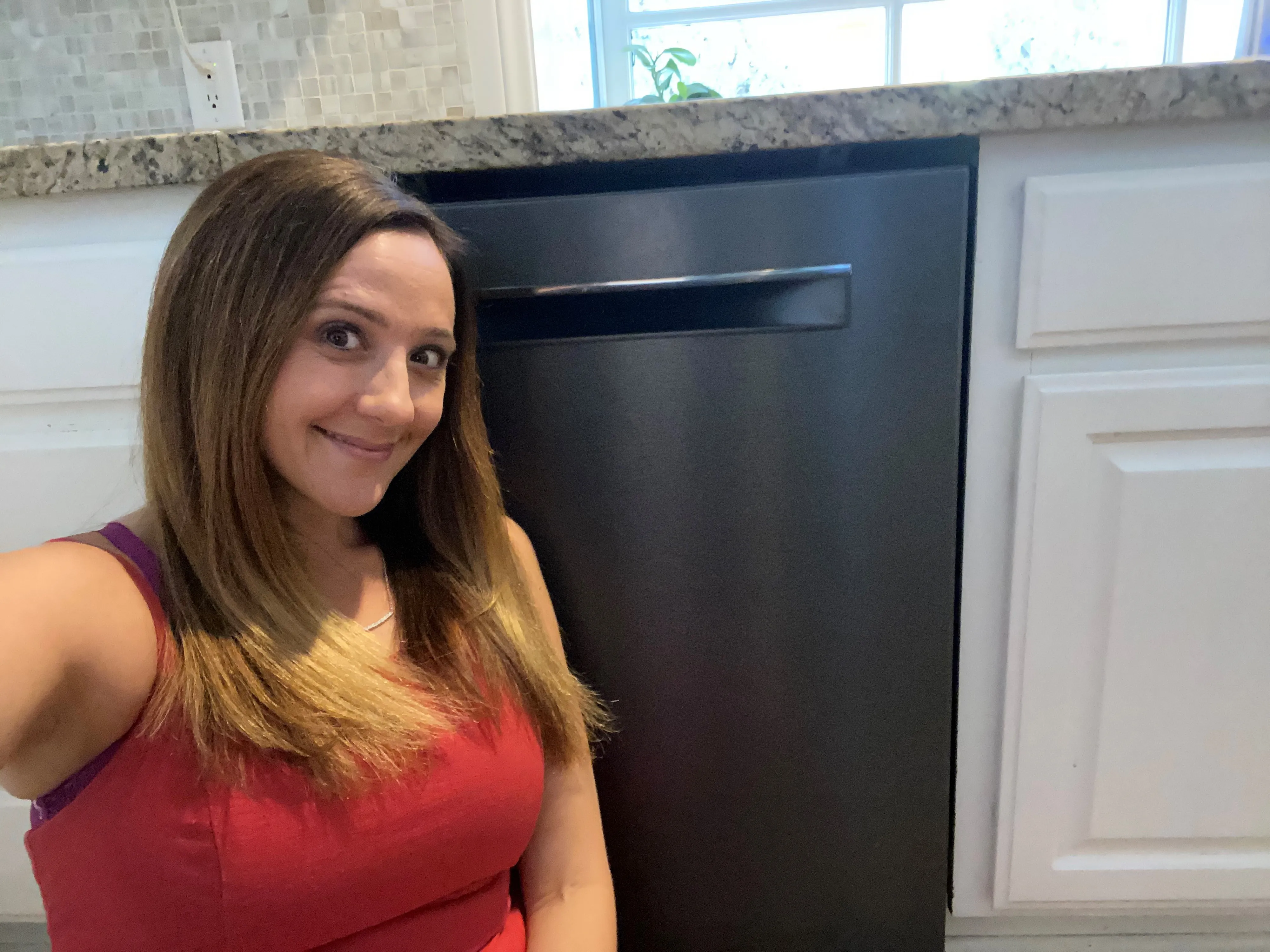 Smiling woman sitting on a kitchen floor next to a Bosch stainless steel dishwasher.
