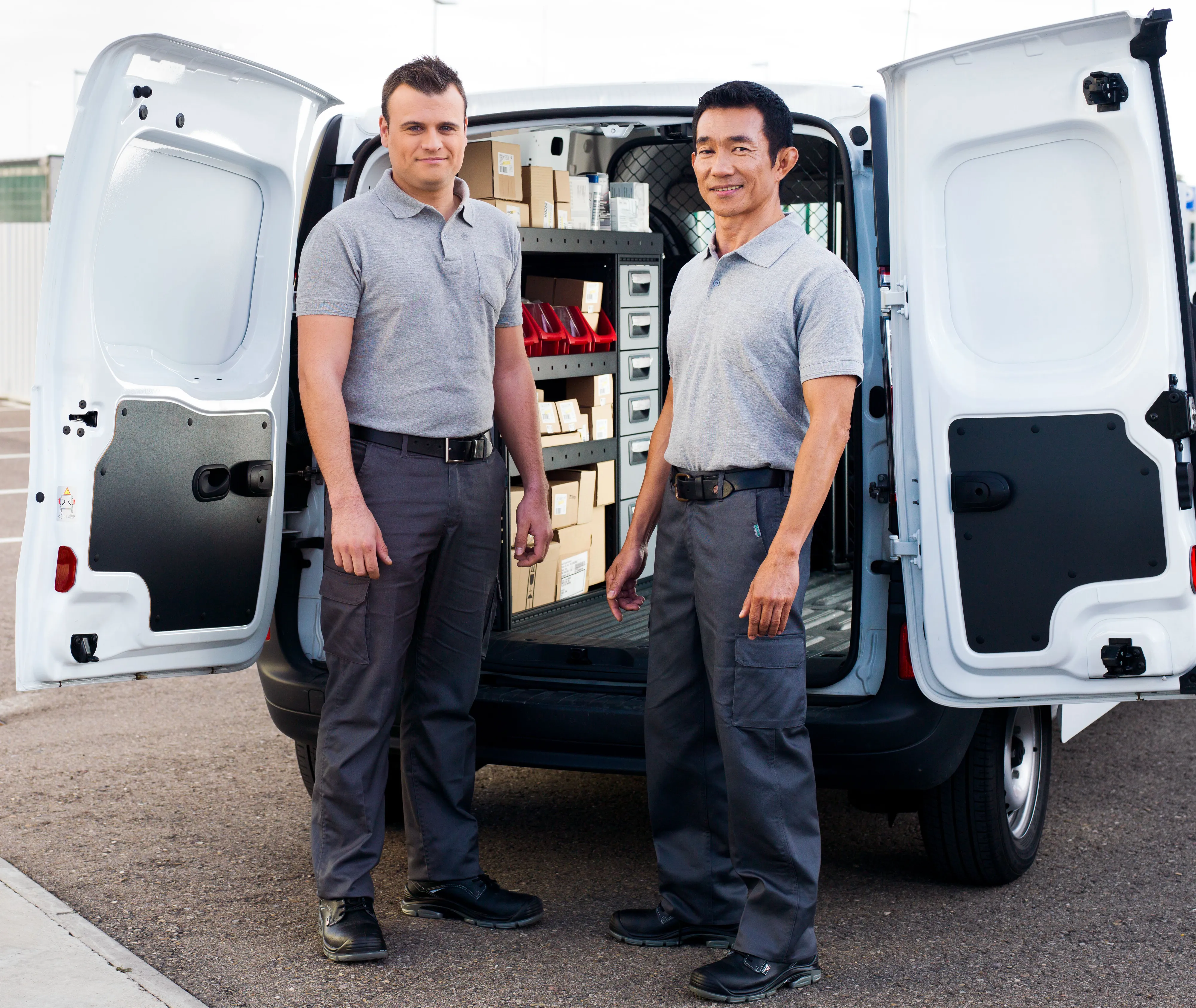 Two workers in uniforms standing beside an open van filled with organized storage boxes.