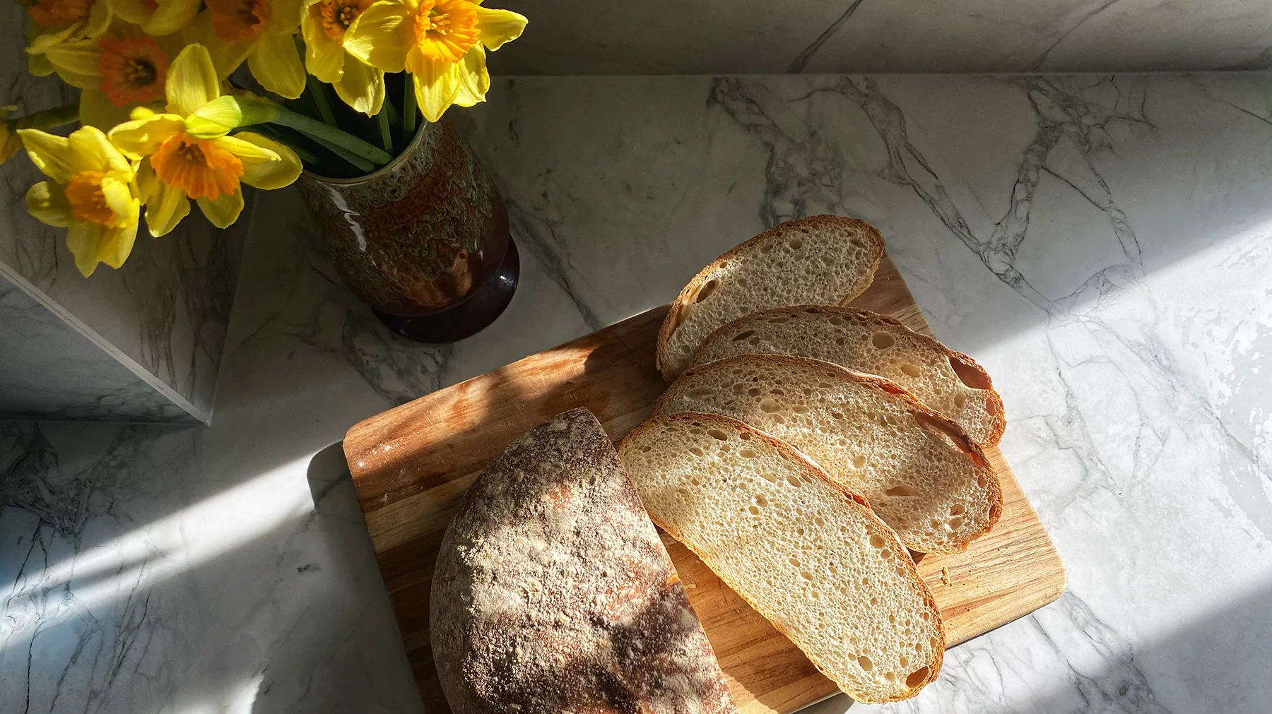 Frisch gebackener Brotlaib mit knuspriger Kruste, aufgeschnitten in mehrere Brotscheiben auf einem Holzbrett