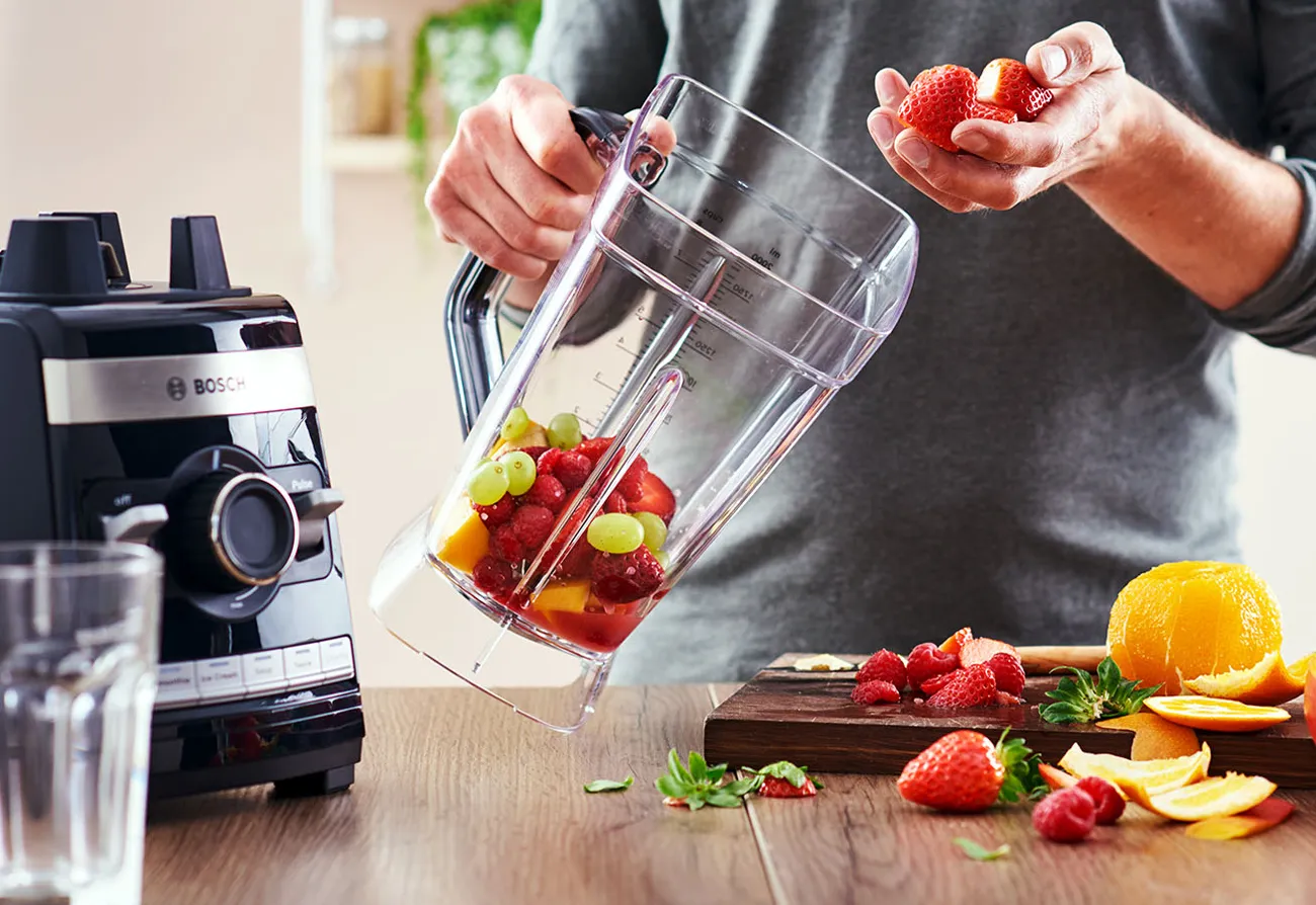 Persoană care amestecă fructe proaspete într-un blender pe blatul de bucătărie.