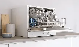 Maşina de spălat vase deschisă cu vase curate pe masa din bucătărie.