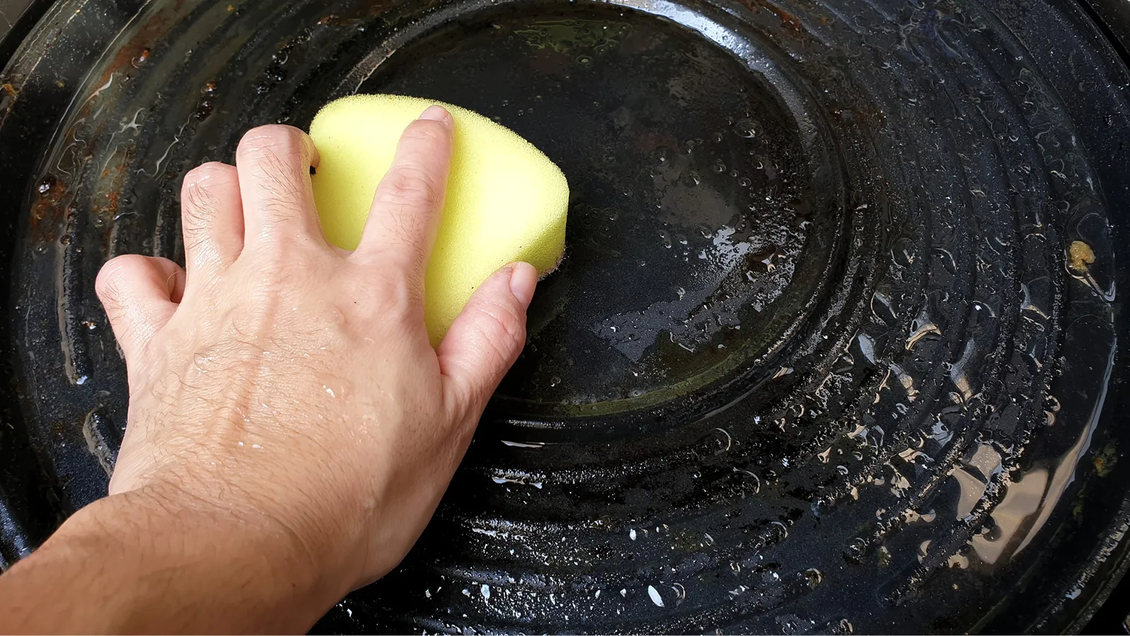 Person using baking soda and vinegar to clean a pan with sponge
