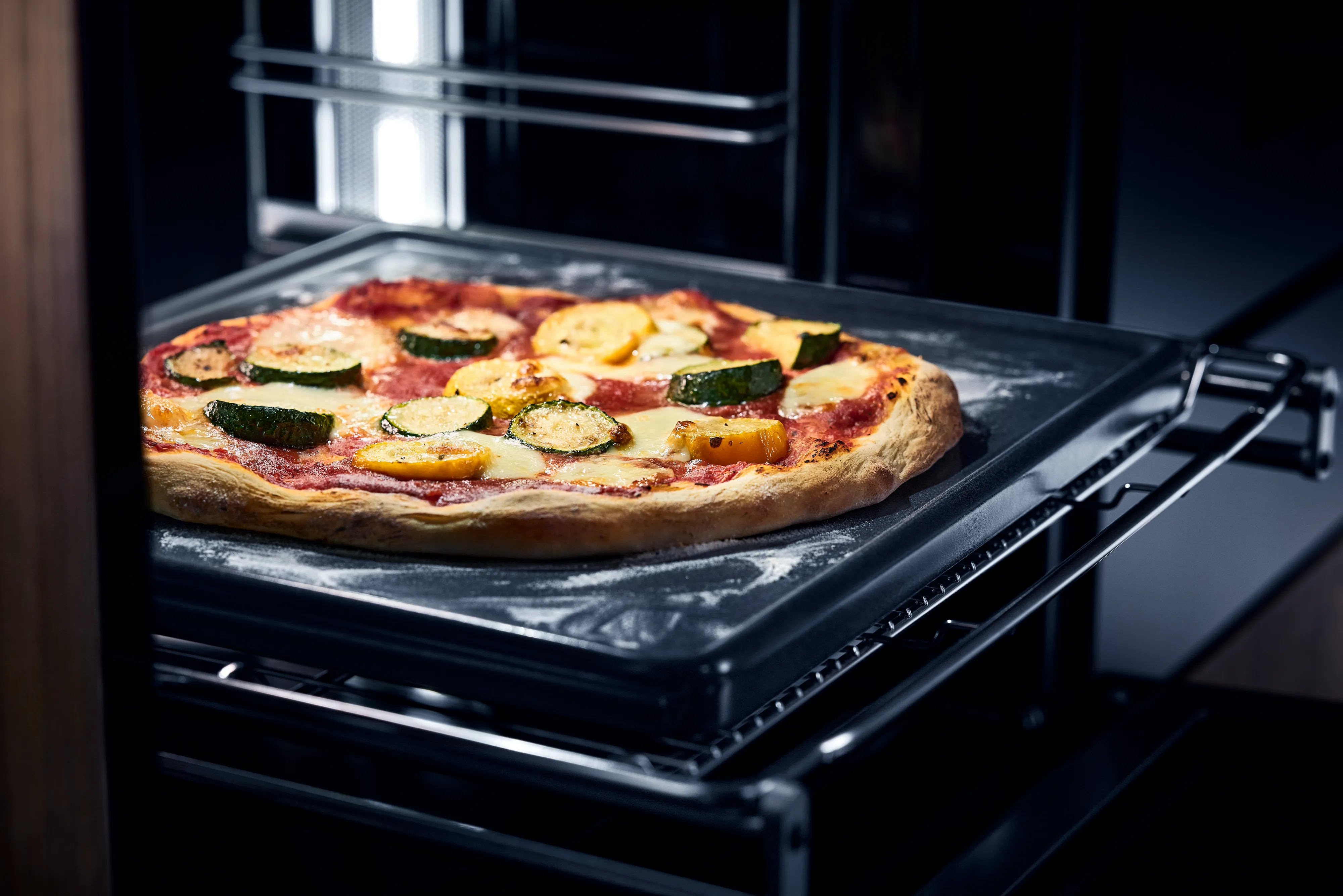 Kabak ve peynirle hazırlanmış bir pizza, fırın tepsisinde fırından kısmen dışarı çekilmiş halde görülüyor.