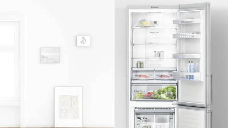 Open refrigerator with fresh produce, shelves, and appliances in a minimalist white room.