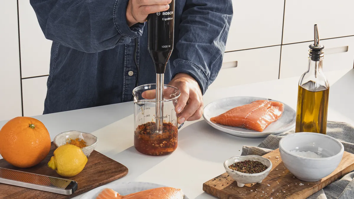 Person preparing salmon dish with various ingredients on kitchen counter.