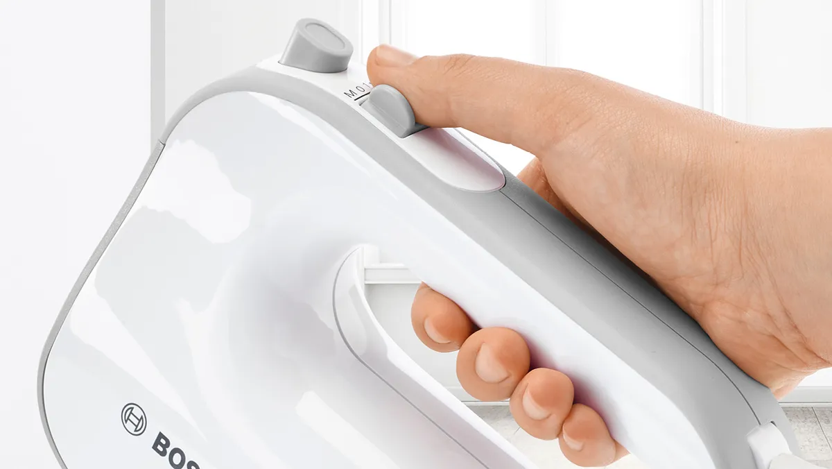 Closeup of a hand holding a Bosch hand mixer with SoftTouch coating, for good grip.