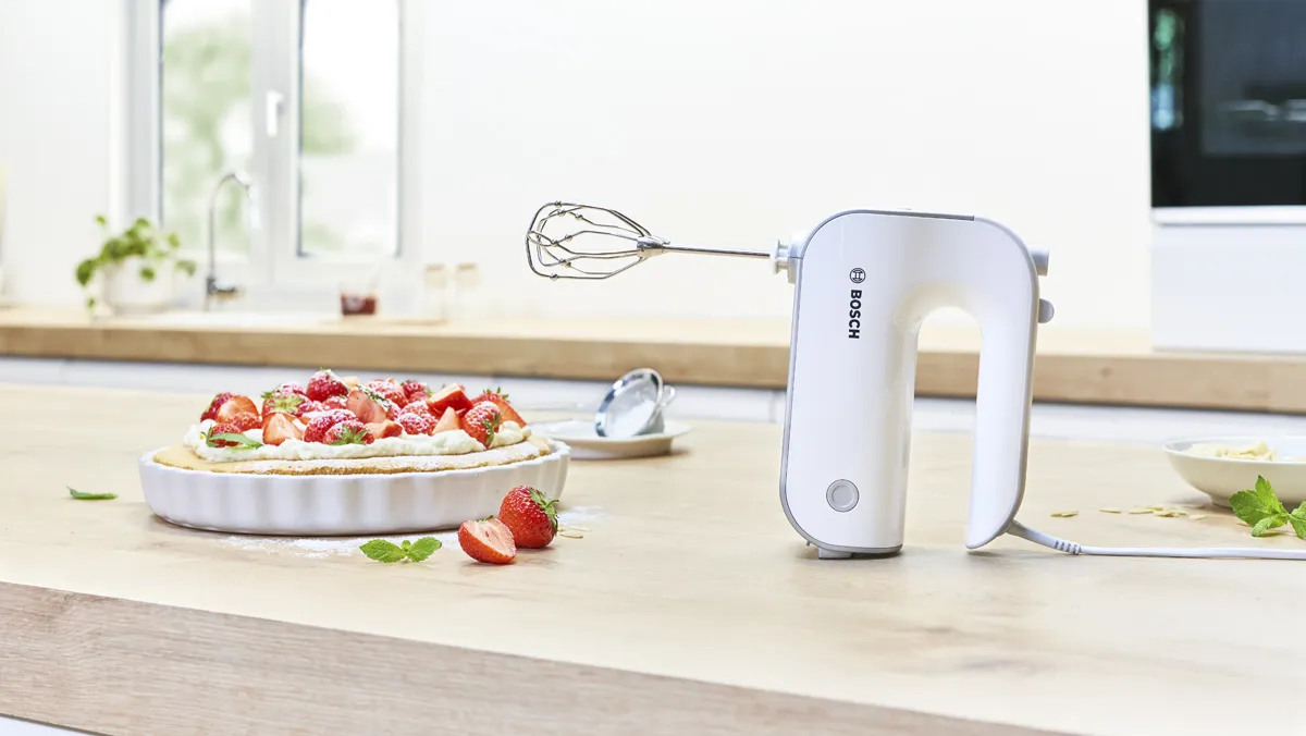 Kitchen counter with electric hand mixer, baking dish with strawberry dessert, and kitchen window.