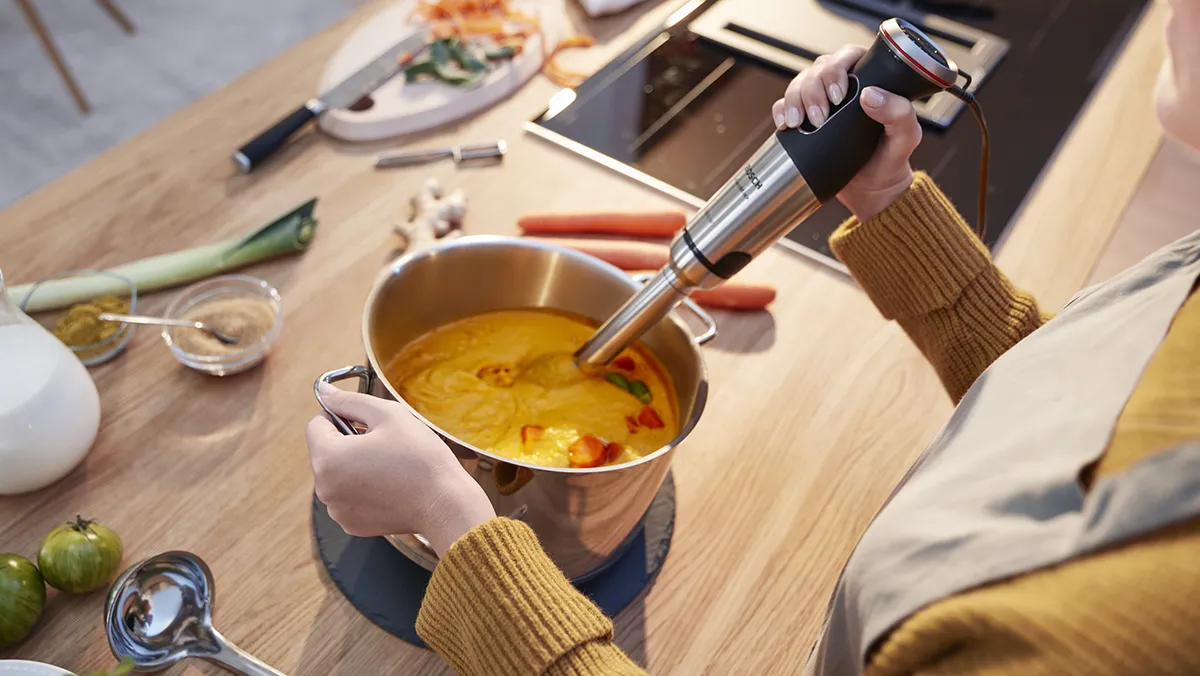 Une femme mixe une soupe orange crémeuse avec un mixeur plongeant Bosch.