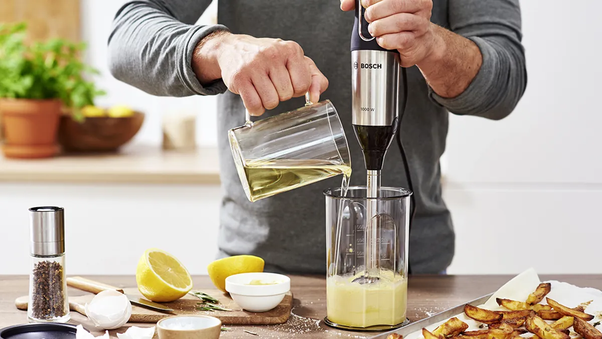Uomo che utilizza frullatore per preparare un drink con limone, erbe e altri ingredienti sul contatore della cucina.
