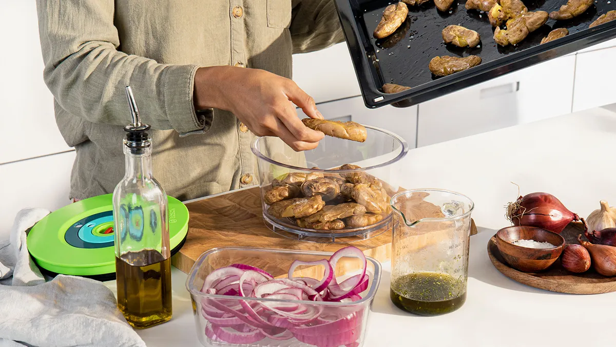 Une personne transfère des aliments cuits d'une plaque de cuisson dans un récipient sous vide.