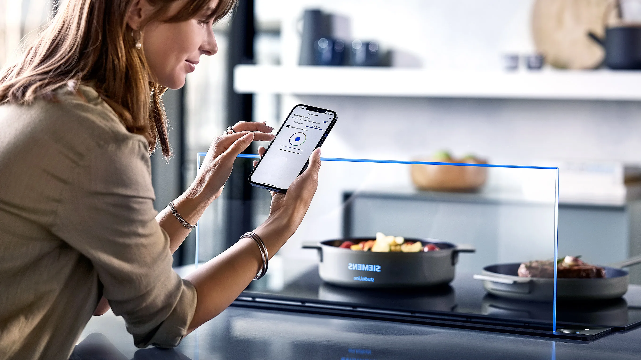 Woman using smartphone to control smart home appliances in modern kitchen.