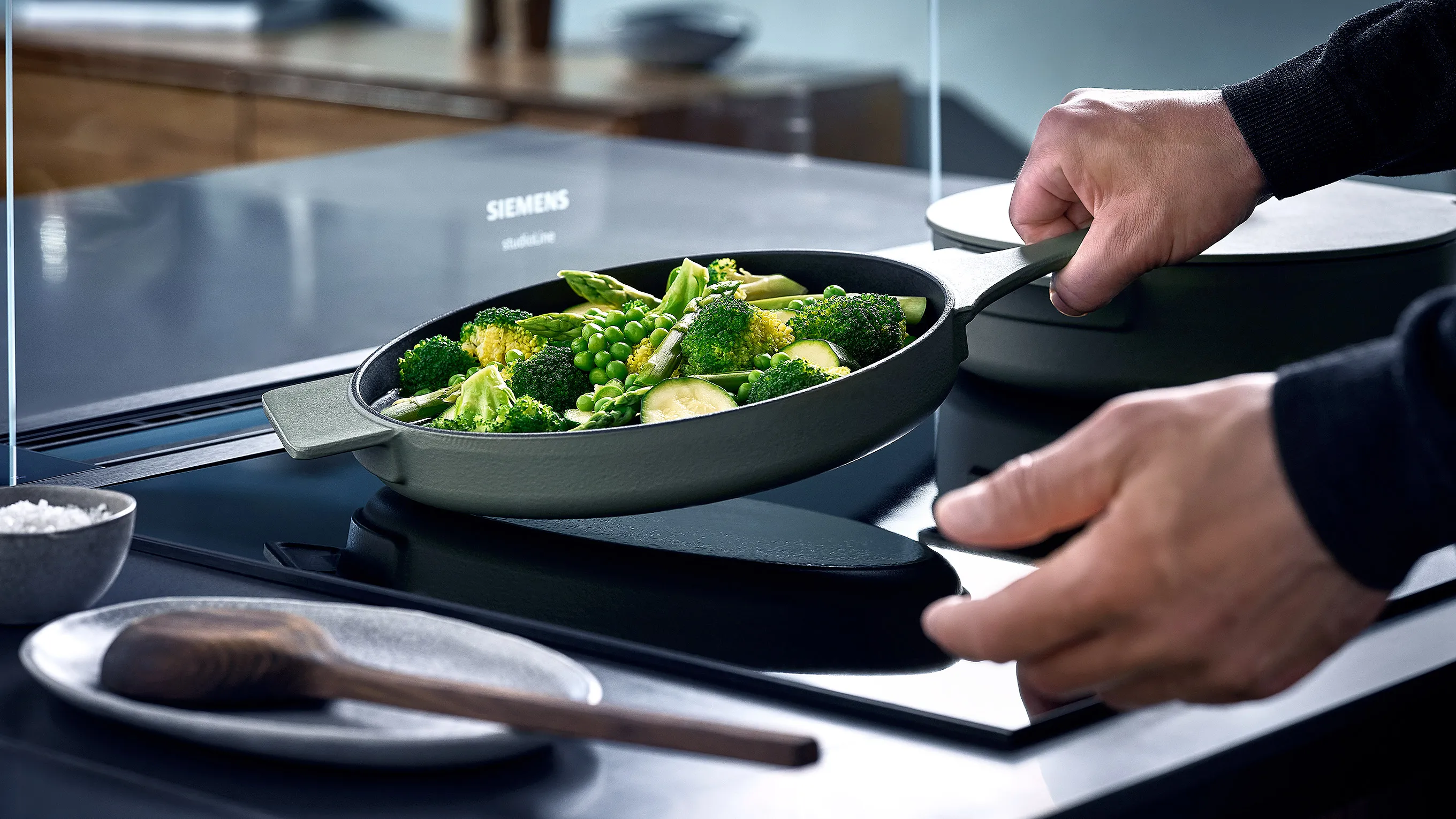 A frying pan with sizzling food sits on a sleek induction cooktop, emitting steam in a modern kitchen setting.