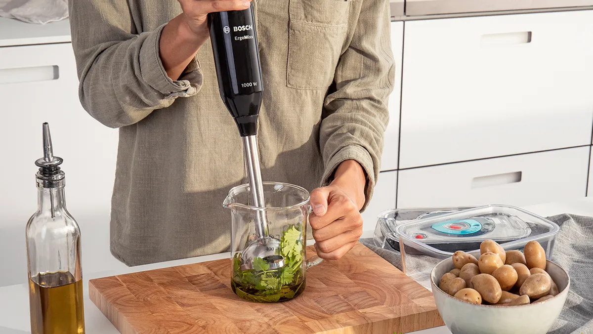 A person standing at worktop using a Bosch hand blender to puree in a beaker.