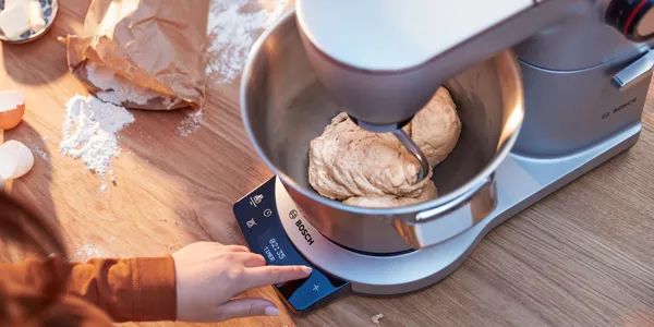 Robot pâtissier pétrissant une pâte, main sur la commande, farine et coquilles sur le plan de travail.