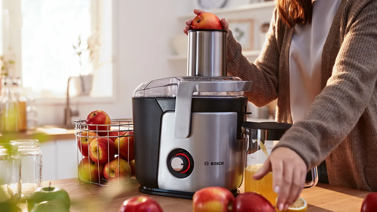 A person standing at a kitchen worktop puts apples into a Bosch juicer.