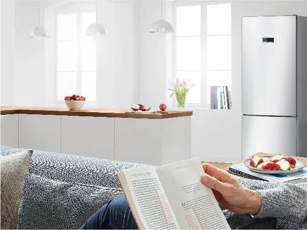 Person on sofa reading in front of fridge freezer