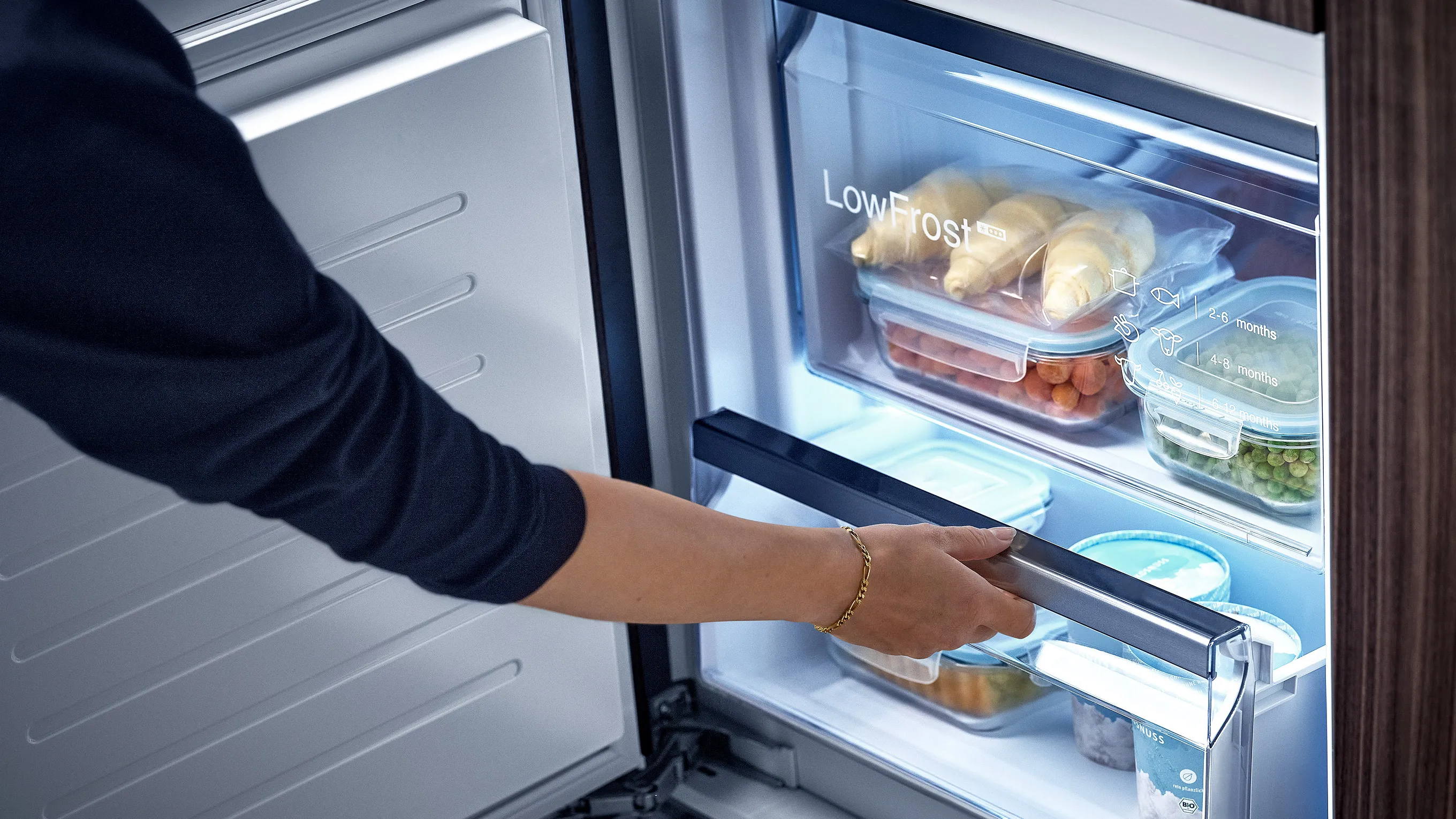 Person opening refrigerator with various food items inside.