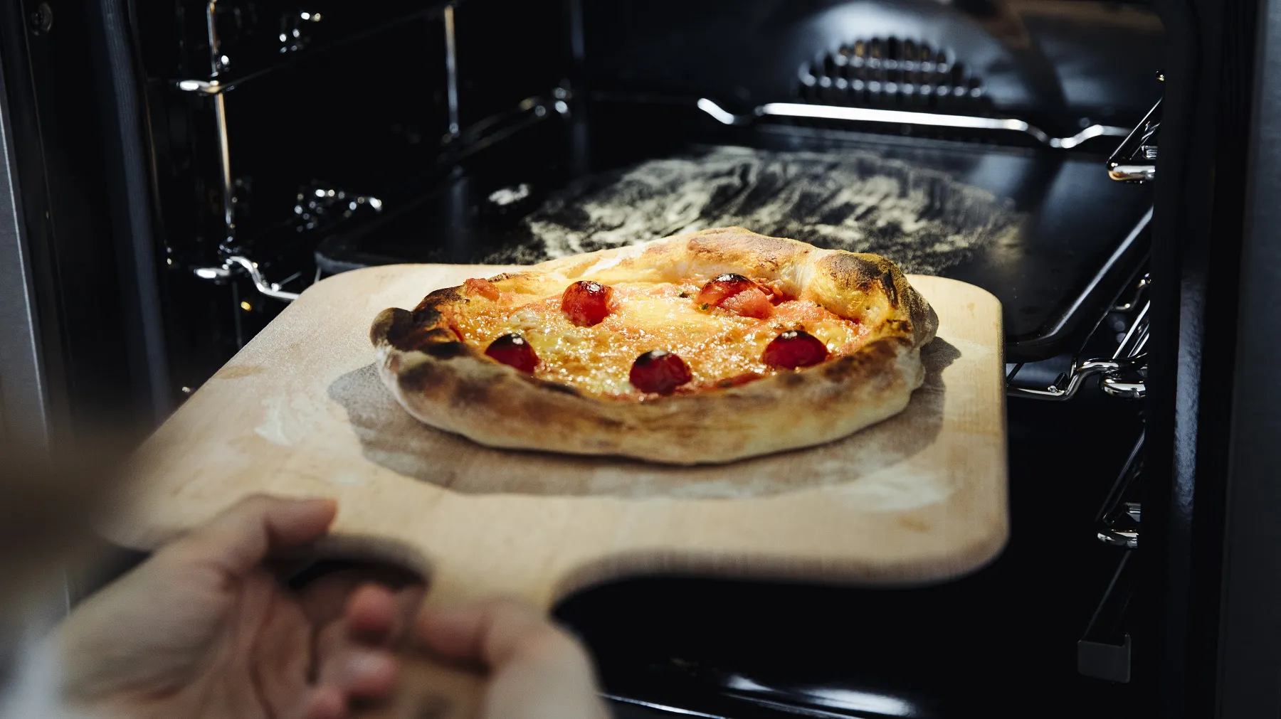 Pizza mit Tomatensauce und Käse auf einem Holzbrett wird in einen Ofen geschoben