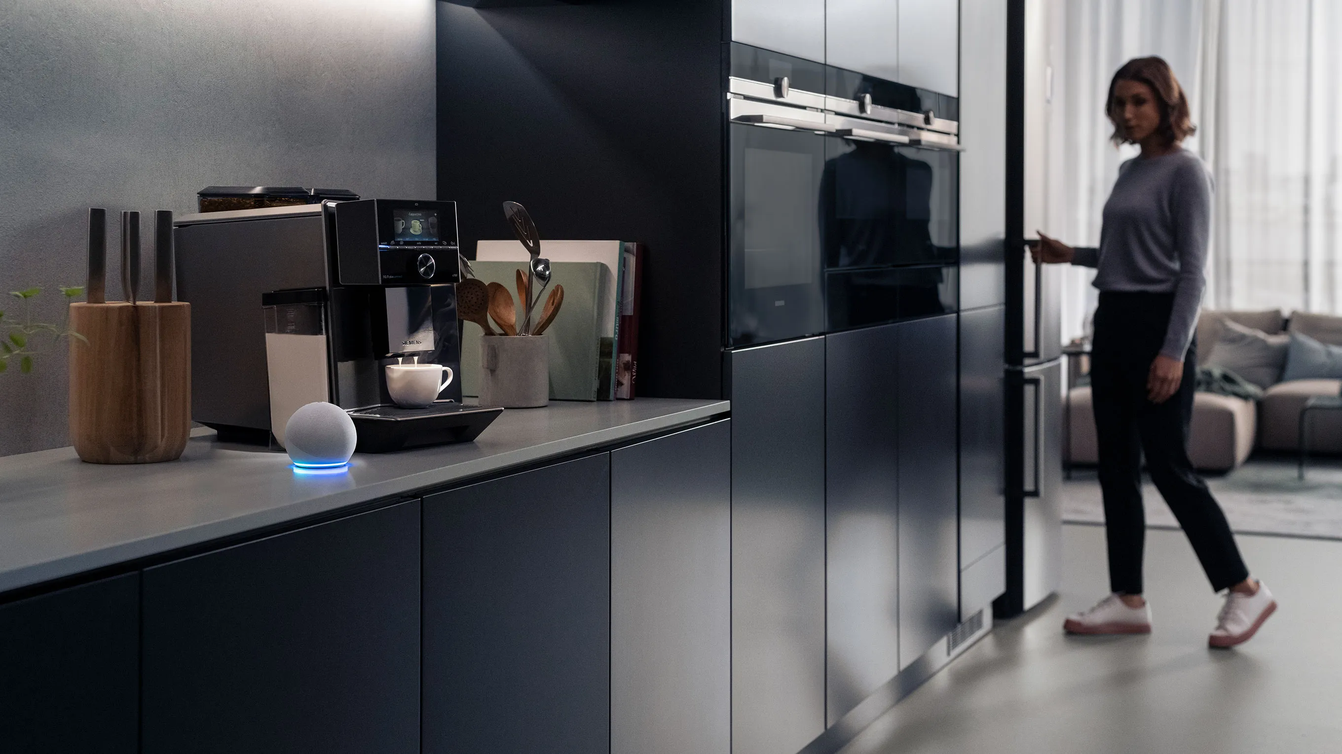 Amazon echo in the kitchen by Siemens coffee machine, with a woman opening a cupboard door