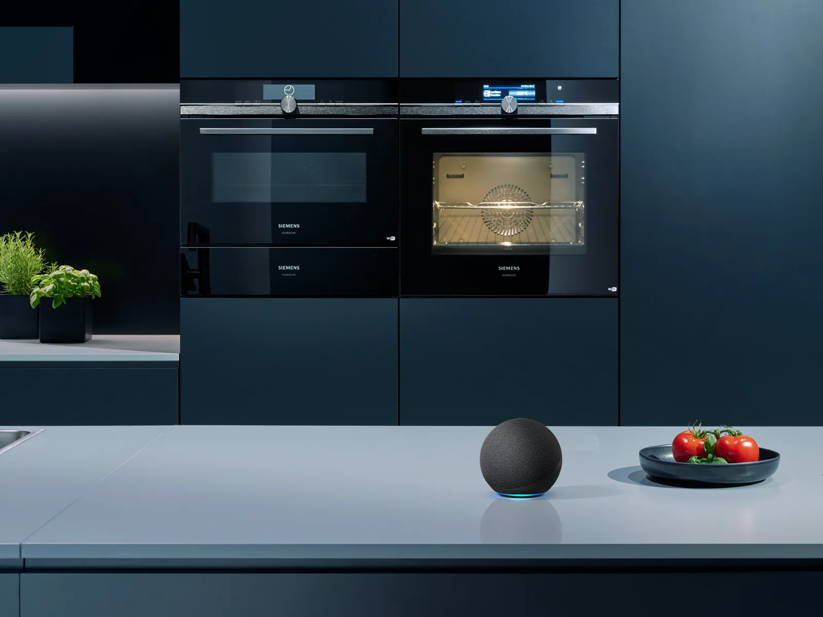 Una cucina moderna con forni da incasso Siemens, un altoparlante intelligente sul piano di lavoro e una ciotola di pomodori freschi e basilico.