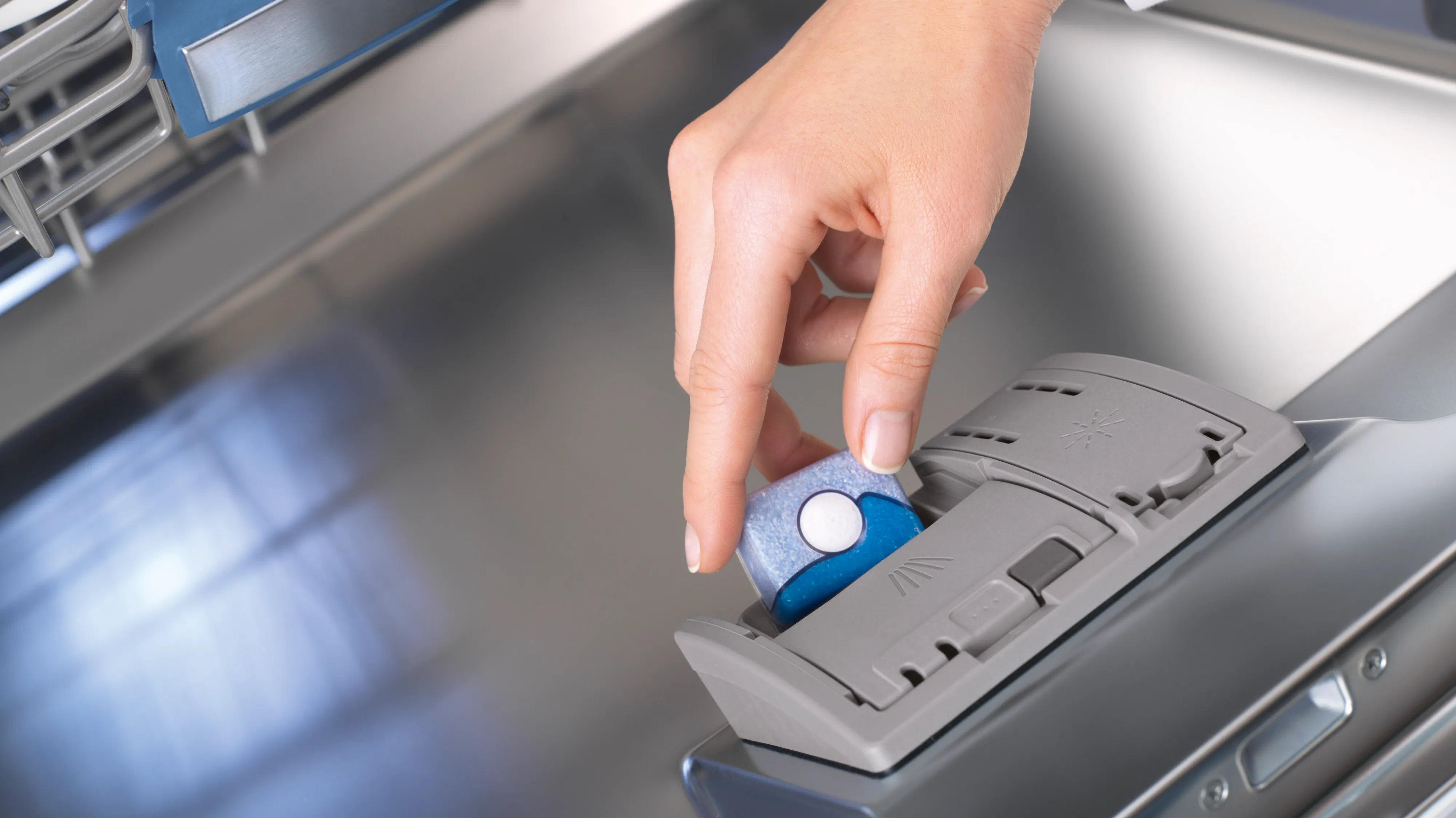 Hand placing detergent pod in Bosch dishwasher, cleaning appliance.