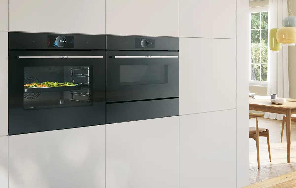 A Bosch built-in oven with vegetables inside next to a built-in microwave.