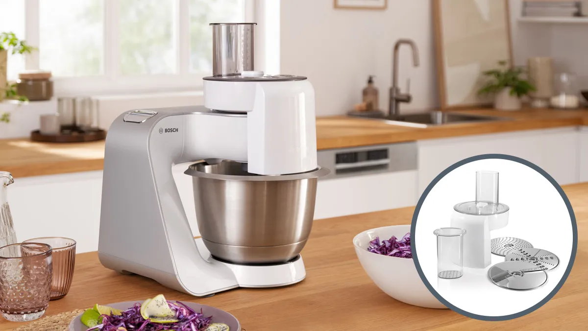 A modern Bosch kitchen mixer in a bright kitchen, featuring a stainless steel bowl and a bowl with attachments displayed in an inset.