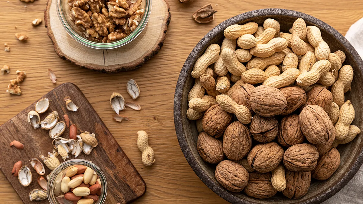 Assorted nuts and seeds on wooden surface, including walnuts, almonds, and peanuts.