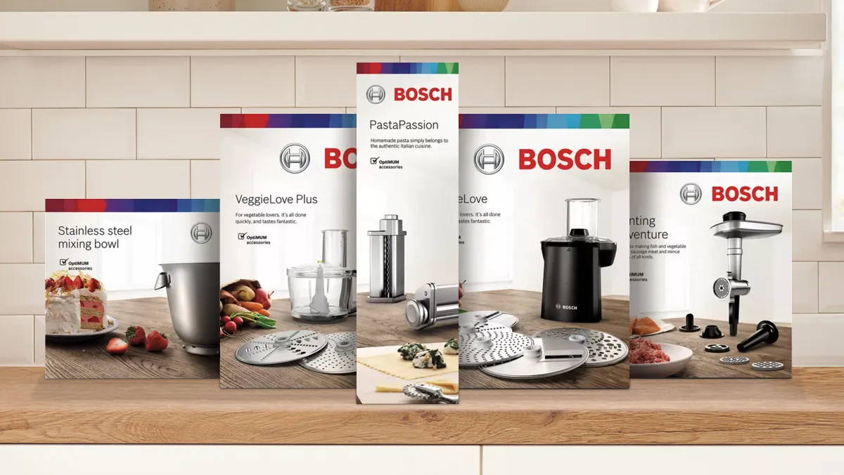 Aparate de bucătărie Bosch, inclusiv castron de amestecare, filtru de paste, feliat de legume, și tocător de carne afișate pe suprafața de lemn.