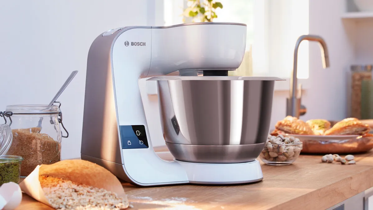Bosch Serie 4 köksmaskin med en metallskål på en träbänk, omgiven av ingredienser.