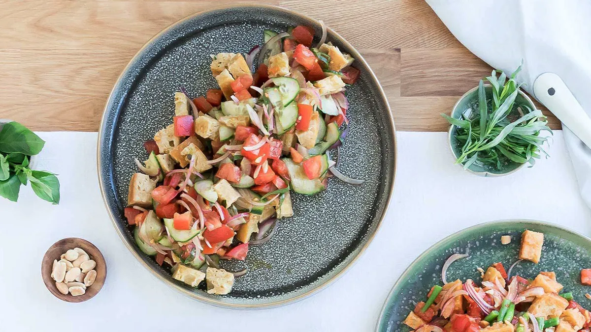 Top-down view of a salad with cucumbers, tomatoes, croutons, and greens on a speckled plate.