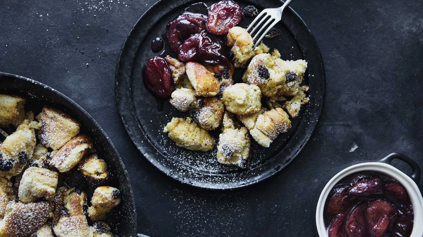Teller mit Kaiserschmarrn und Zwetschgenröster, daneben Schüssel mit Zwetschgenkompott auf dunklem Untergrund