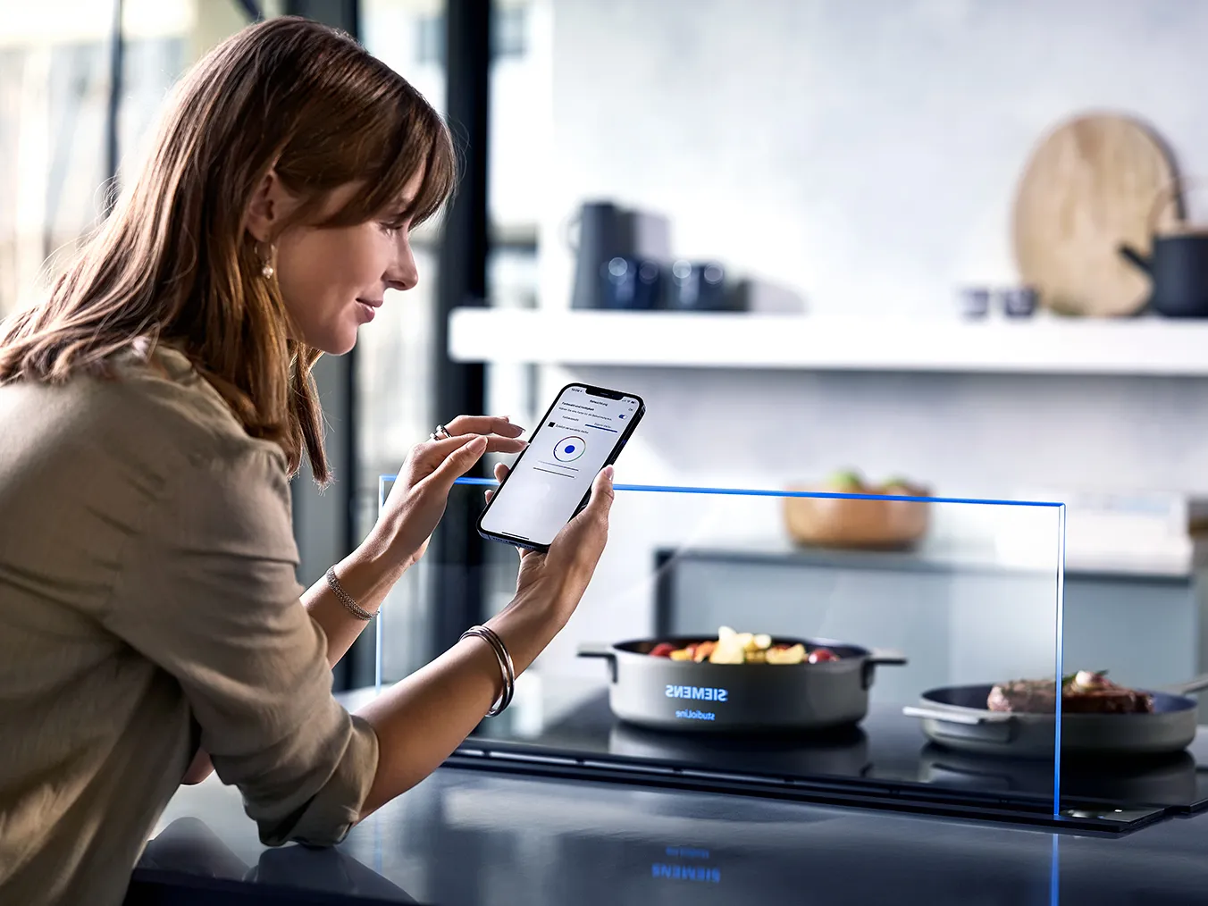 Woman using smartphone in modern kitchen with cooking appliances.