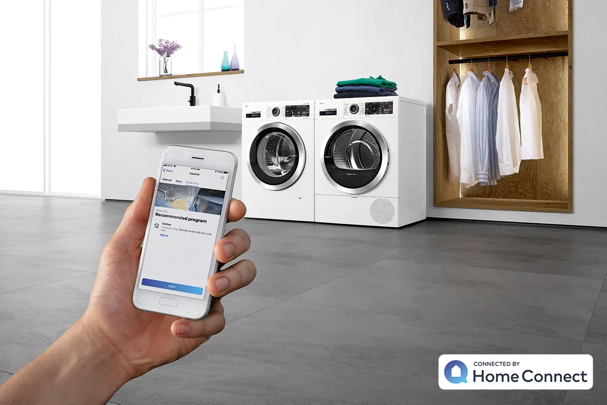 Hand holding smartphone controlling smart home appliances on kitchen wall.