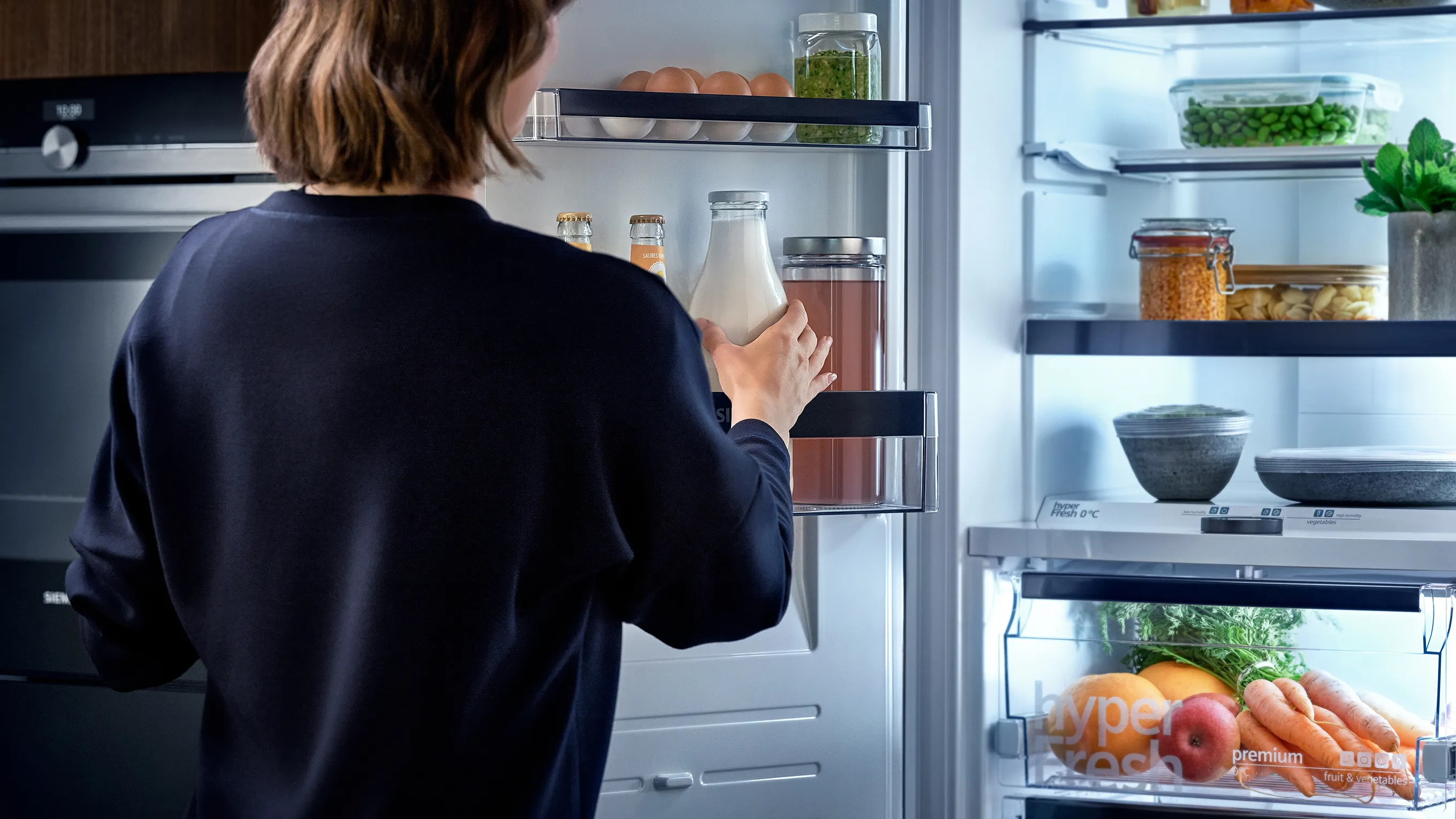 Person looking inside open refrigerator, shelves stocked with various food items.
