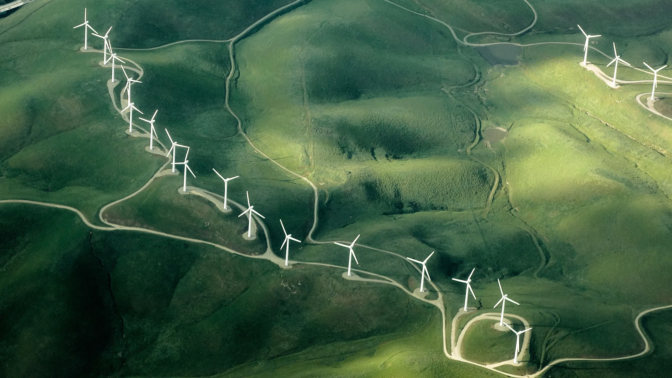 Aerial view of a wind farm with turbines on rolling green hills, symbolising renewable energy and sustainability.