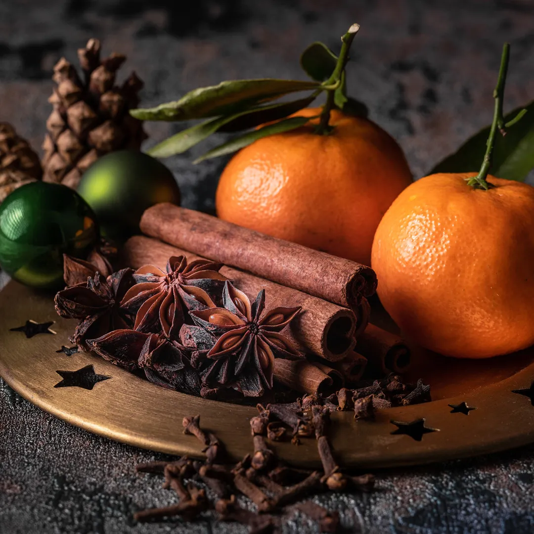 Citrus fruits, cinnamon sticks, star anise, cloves, dark background, seasonal spices.