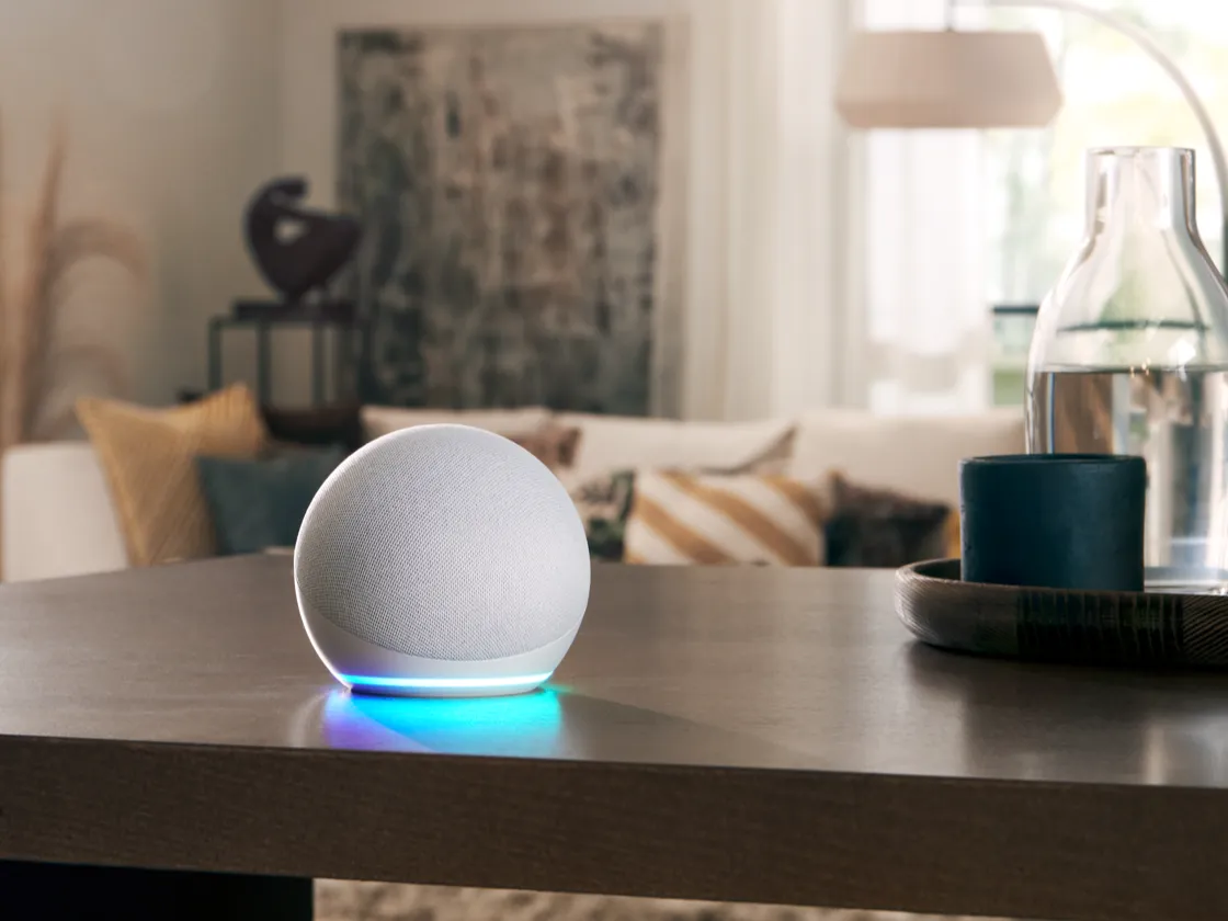 White spherical smart speaker with a glowing blue LED base sitting on a table in a softly lit living room.