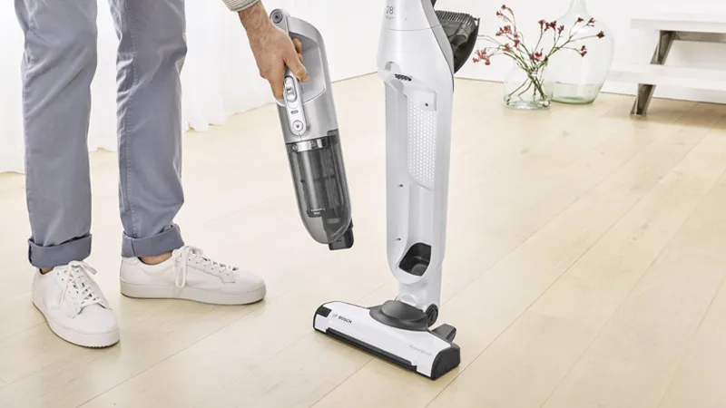 Person using vacuum cleaner to clean hardwood floor in home.